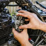 Ręce mechanika regulują gaźnik motocykla, pokazując, jak działa ssanie.
