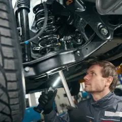 Mechanik bada elementy zawieszenia samochodu podniesionego na podnośniku, oświetlając je latarką.