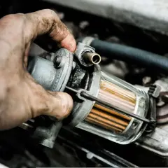 Brudna ręka mechanika trzyma filtr paliwa. Zapchany filtr gazu objawy mogą być różne, np. nierówna praca silnika.