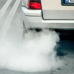 Z tyłu samochodu wydobywa się gęsty, biały dym z wydechu, tworząc obłok na drodze.
