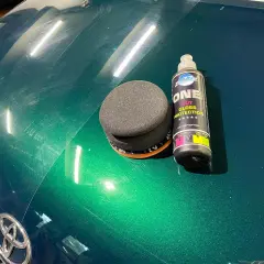 Zestaw do ręcznego polerowania auta: gąbka i butelka z preparatem "ONE CUT GLOSS PROTECTION". Widać zarysowania na zielonym lakierze.
