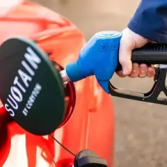 Tankowanie czerwonego samochodu paliwami syntetycznymi. Dystrybutor z logo "SUOTAIN" jest wkładany do wlewu paliwa.