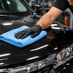 Ręka w czarnej rękawiczce poleruje czarny lakier auta niebieską mikrofibrą. Czy po woskowaniu płukać auto? To pytanie zadaje sobie wielu kierowców.