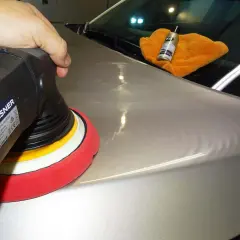 Nakładanie powłoki ceramicznej na lakier samochodu za pomocą polerki. Pomarańczowa ściereczka i buteleczka z preparatem K2 na masce.
