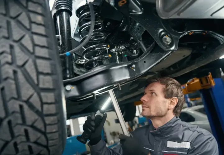 Mechanik bada elementy zawieszenia samochodu podniesionego na podnośniku, oświetlając je latarką.