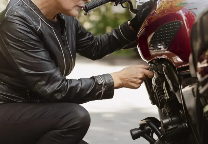 Kobieta w skórzanej kurtce sprawdza, ile pali motocykl, dotykając kluczyka zapłonu.