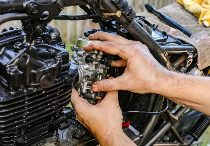 Ręce mechanika regulują gaźnik motocykla, pokazując, jak działa ssanie.