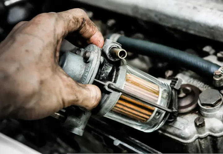 Brudna ręka mechanika trzyma filtr paliwa. Zapchany filtr gazu objawy mogą być różne, np. nierówna praca silnika.