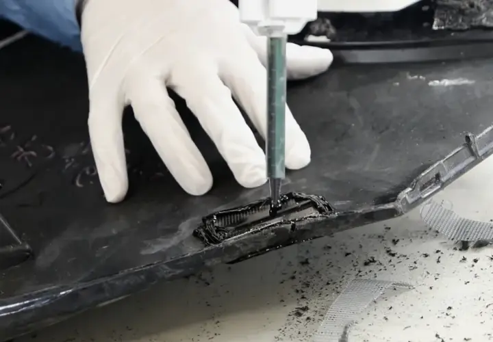 Rękawiczki i strzykawka pomagają w procesie, jak naprawić pęknięty plastik. Widać czarne tworzywo i siatkę wzmacniającą.