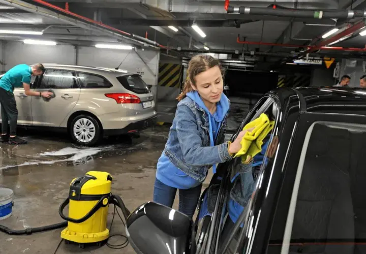 Dziewczyna z żółtą ściereczką poleruje czarne auto. Obok stoi żółty odkurzacz i wiadro. W tle mężczyzna myje srebrne auto. Pokazują, czym umyć auto domowe sposoby.