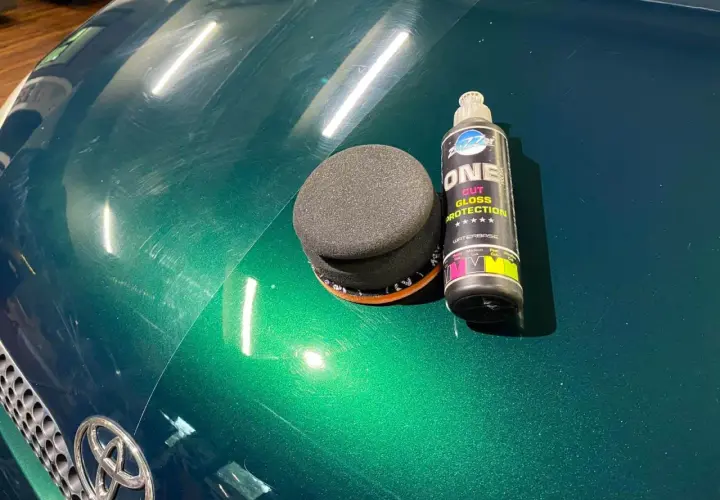 Zestaw do ręcznego polerowania auta: gąbka i butelka z preparatem "ONE CUT GLOSS PROTECTION". Widać zarysowania na zielonym lakierze.