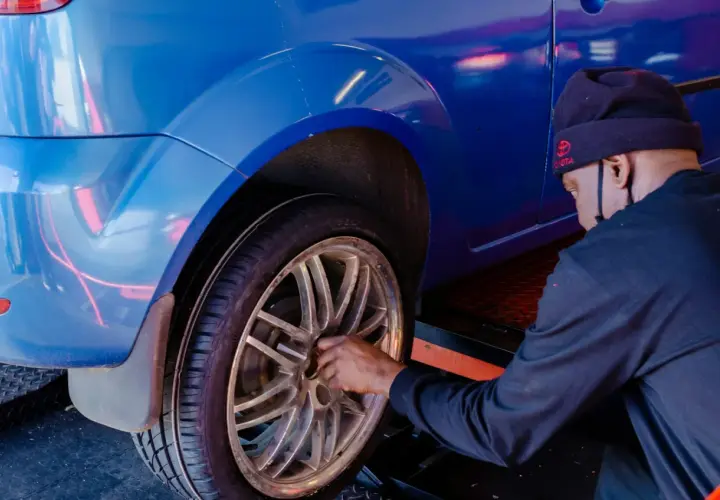 Mężczyzna w czapce z logo Toyoty dokonuje wymiany koła w niebieskim aucie.