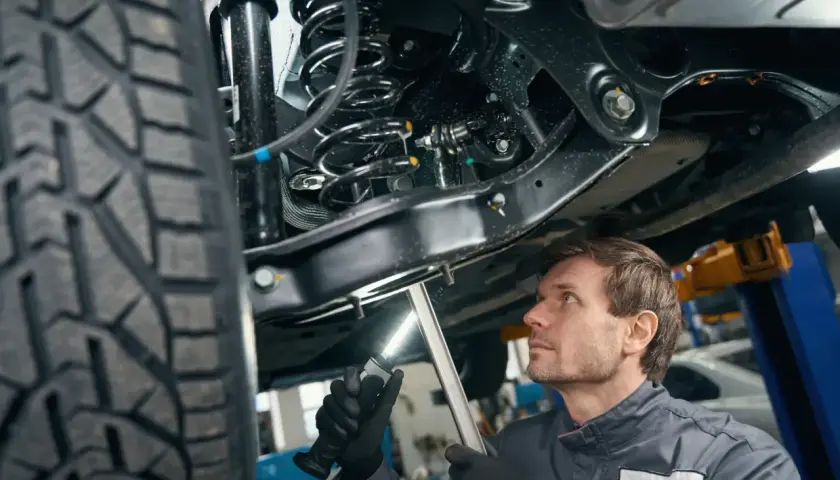 Mechanik bada elementy zawieszenia samochodu podniesionego na podnośniku, oświetlając je latarką.
