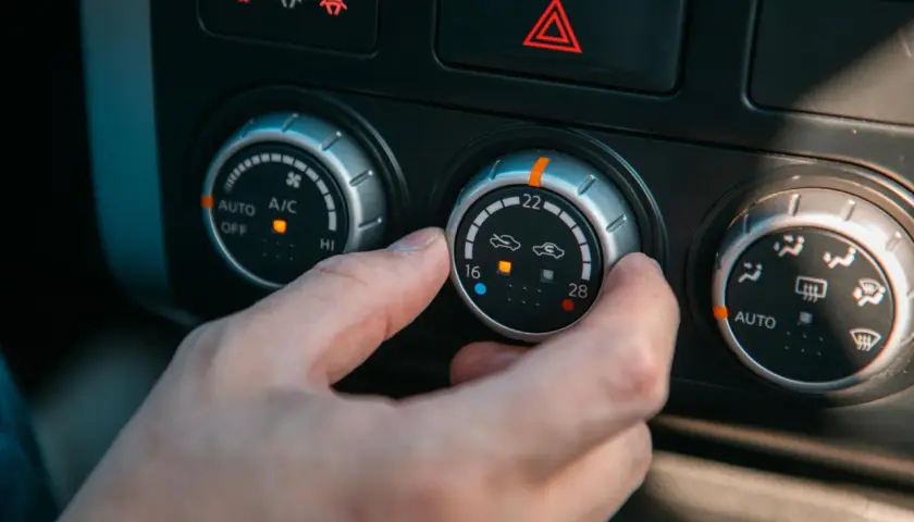 Dłoń reguluje pokrętłem termostat w samochodzie, ustawiając temperaturę na 22 stopnie.