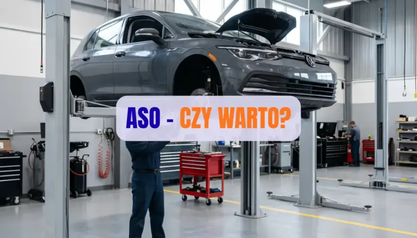 Mechanik pracuje pod samochodem na podnośniku w warsztacie. Napis "ASO - CZY WARTO?" sugeruje dyskusję o serwisach autoryzowanych.