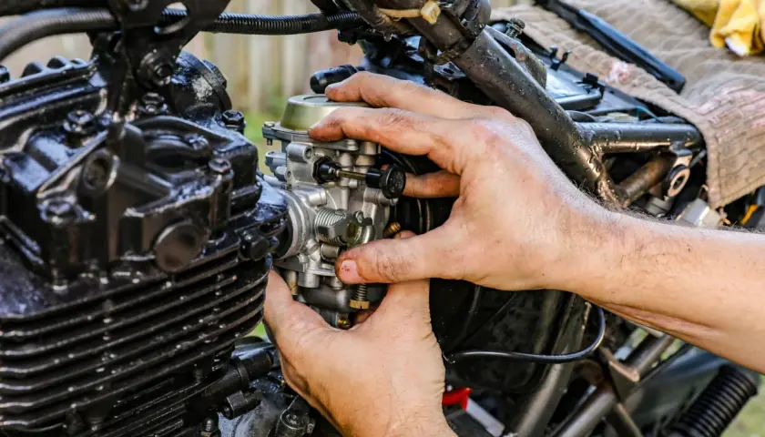 Ręce mechanika regulują gaźnik motocykla, pokazując, jak działa ssanie.