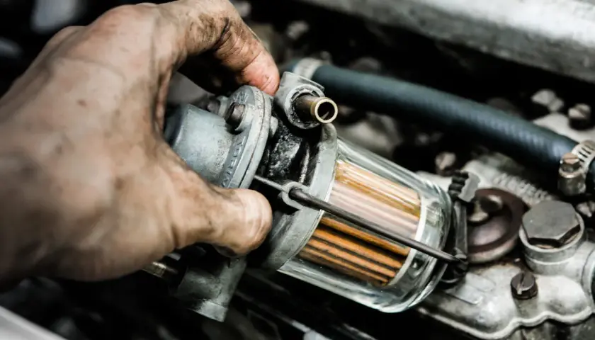 Brudna ręka mechanika trzyma filtr paliwa. Zapchany filtr gazu objawy mogą być różne, np. nierówna praca silnika.