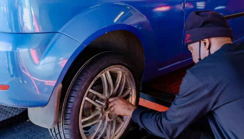 Mężczyzna w czapce z logo Toyoty dokonuje wymiany koła w niebieskim aucie.