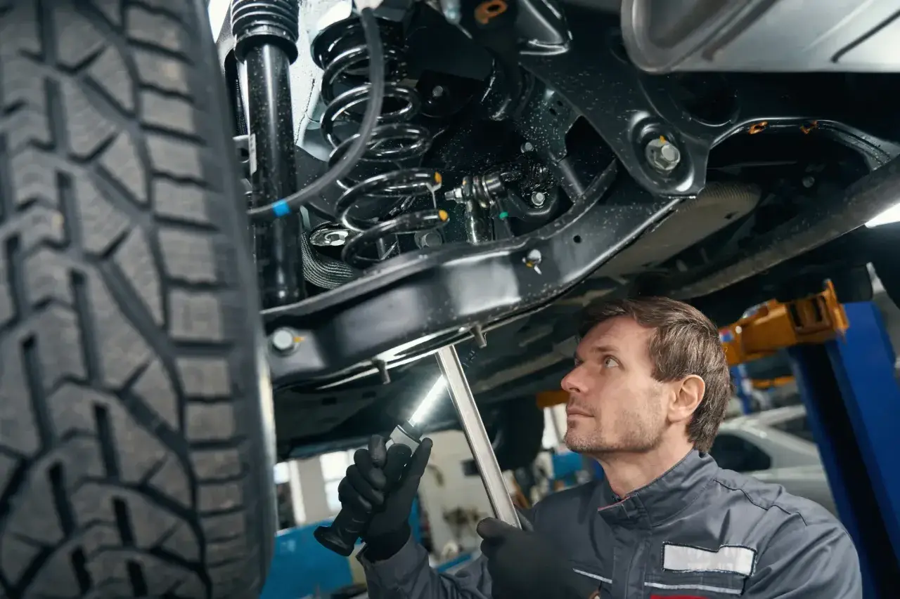 Mechanik bada elementy zawieszenia samochodu podniesionego na podnośniku, oświetlając je latarką.
