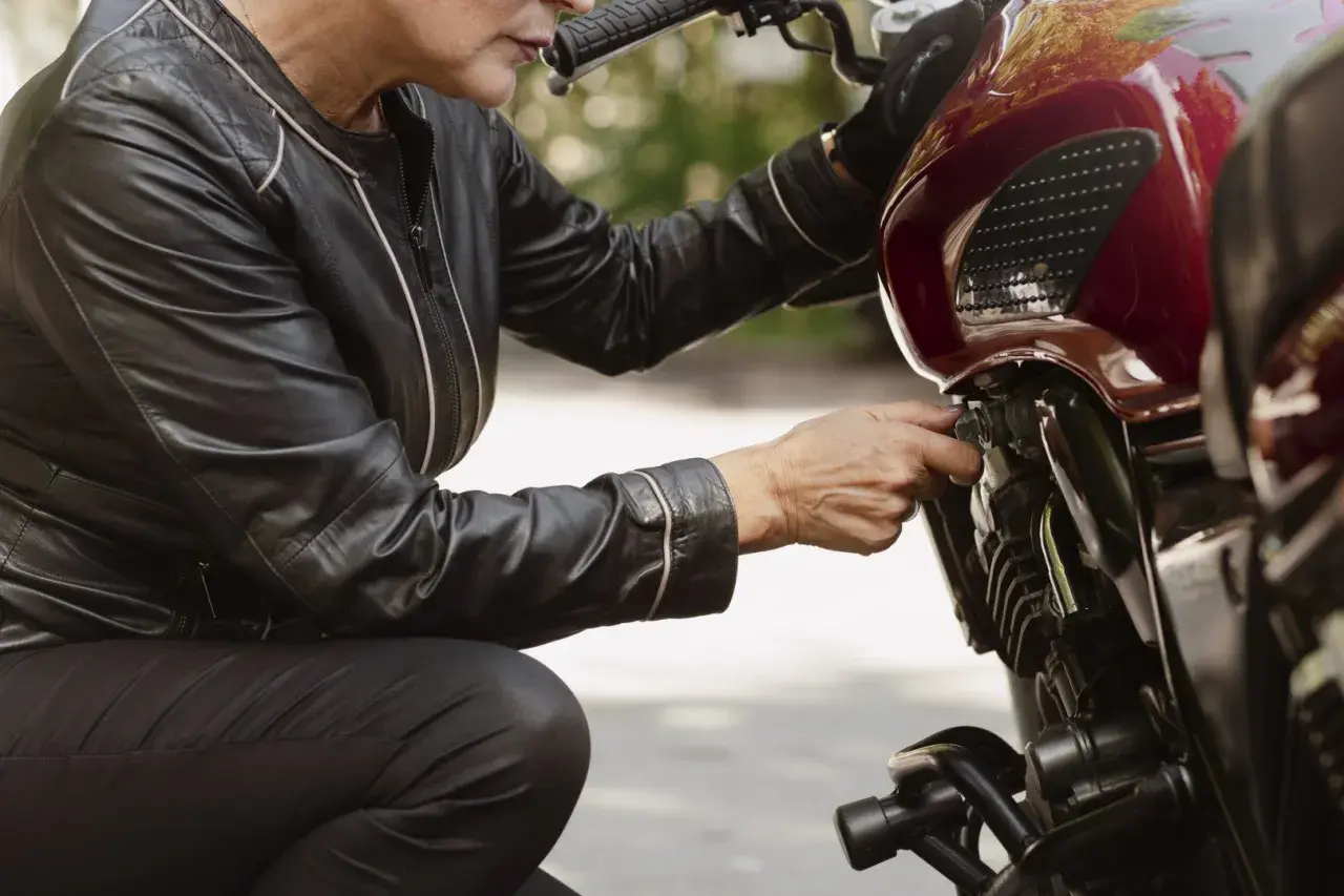 Kobieta w skórzanej kurtce sprawdza, ile pali motocykl, dotykając kluczyka zapłonu.