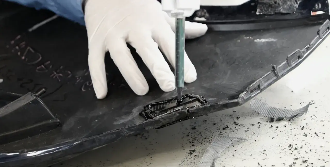 Rękawiczki i strzykawka pomagają w procesie, jak naprawić pęknięty plastik. Widać czarne tworzywo i siatkę wzmacniającą.