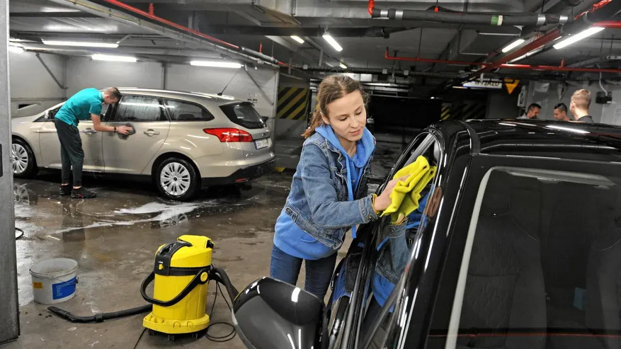 Dziewczyna z żółtą ściereczką poleruje czarne auto. Obok stoi żółty odkurzacz i wiadro. W tle mężczyzna myje srebrne auto. Pokazują, czym umyć auto domowe sposoby.