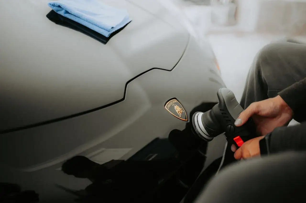Detailowe polerowanie lakieru Lamborghini. Widać rękę z polerką i logo byka. Mikrofibry czekają na dalsze kroki w pielęgnacji.