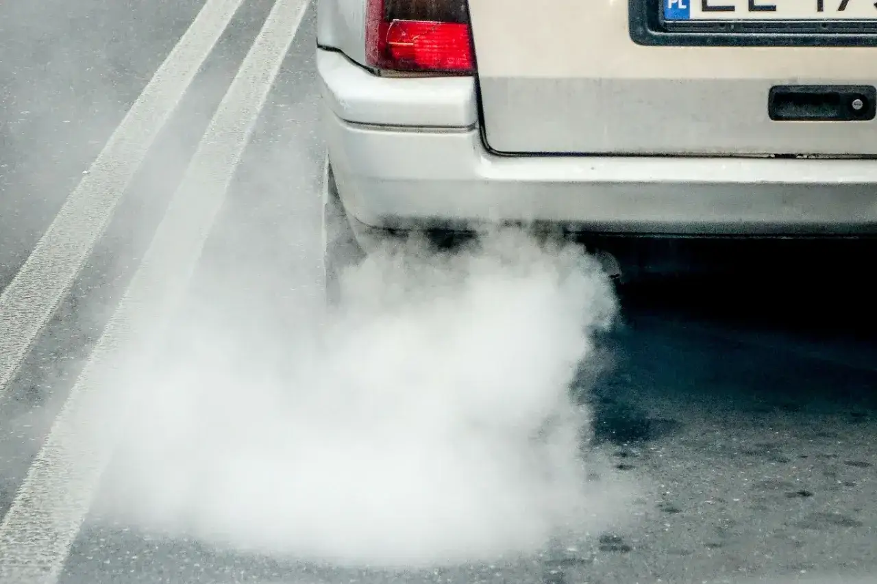 Z rury wydechowej wydobywa się gęsty, biały dym, który zasnuwa asfalt.