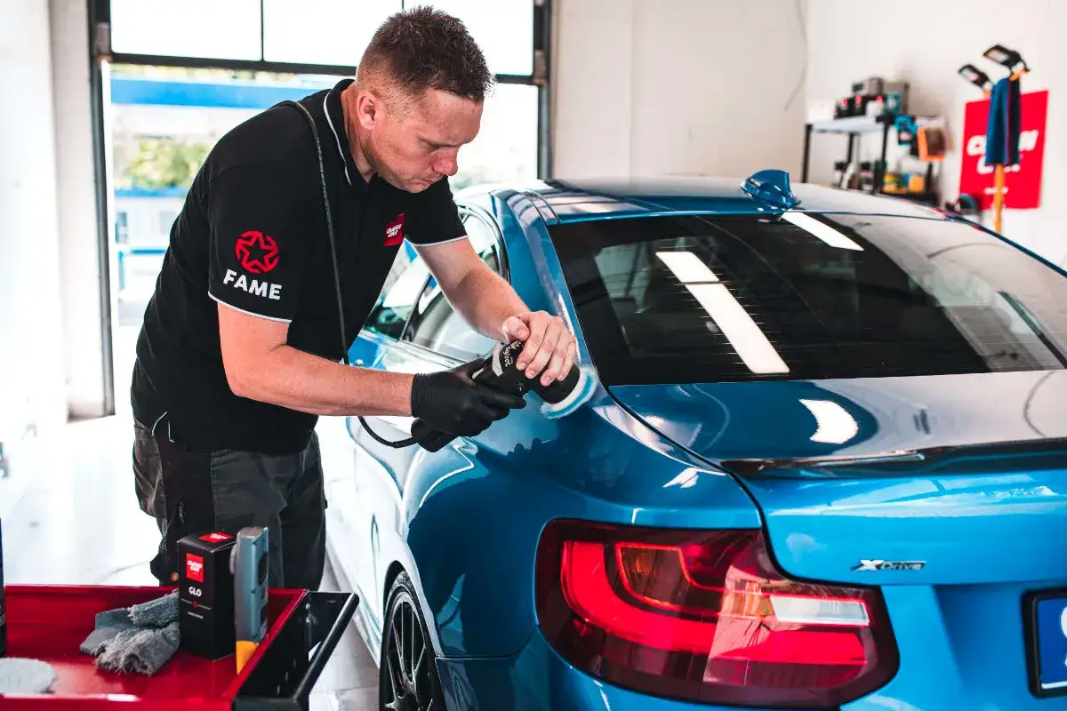 Detailing niebieskiego BMW. Mężczyzna w czarnej koszulce z logo FAME poleruje lakier maszyna.