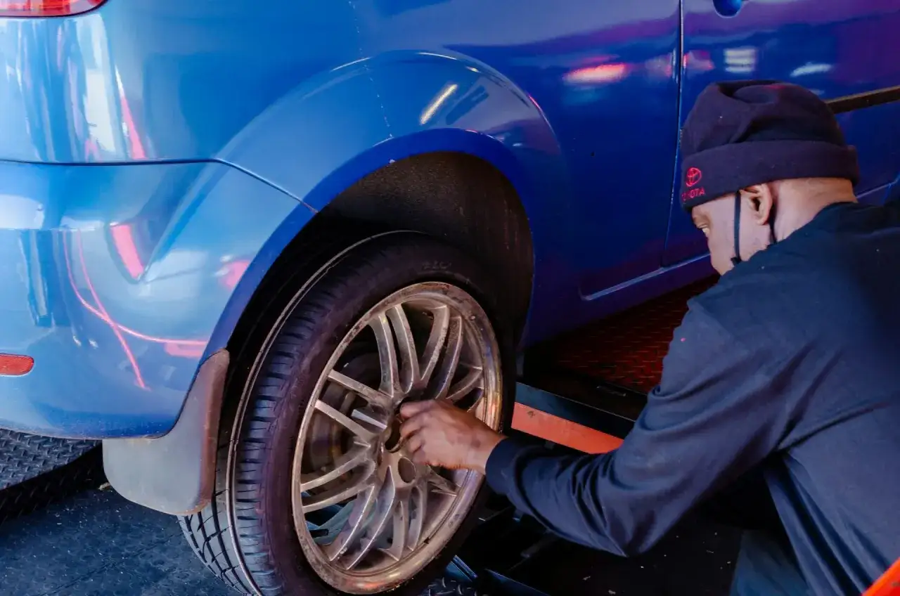 Mężczyzna w czapce z logo Toyoty dokonuje wymiany koła w niebieskim aucie.